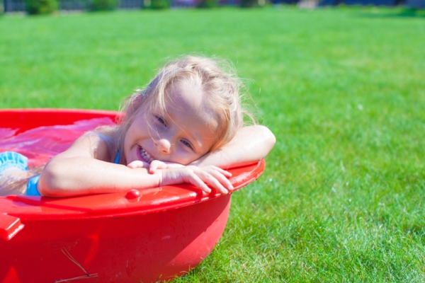 young girl keeping cool during summer while soaked in a plastic tub in the backyard