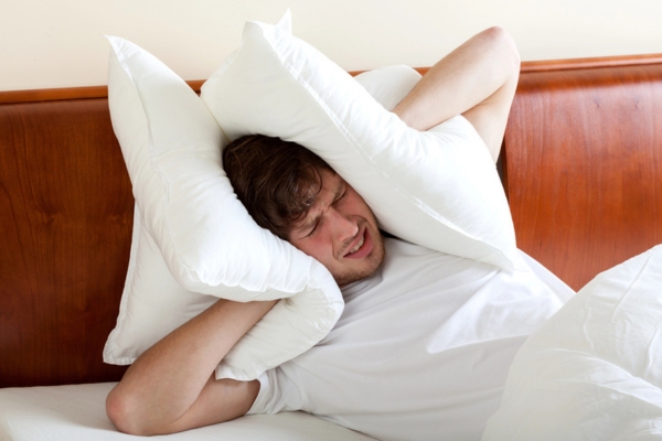 man covering his ears with pillows due to noisy air conditioner