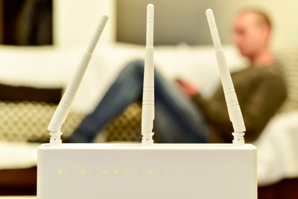 closeup photo of a wireless router with a blurred image of a man behind using mobile phone depicting network connection