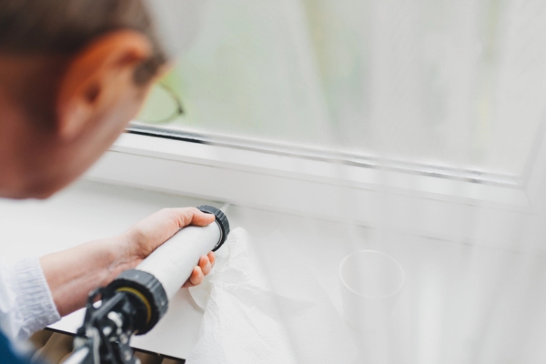 homeowner caulking the home's window to prepare for winter