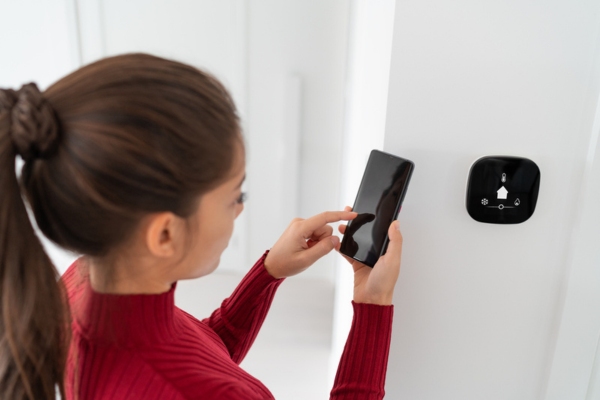 woman synching smart thermostat control for the house on mobile phone