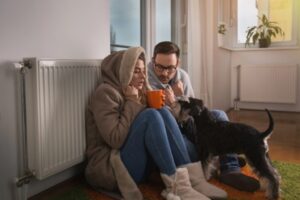 couple and their dog feeling cold lounging by the radiator due to heating system breakdown